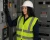 Female electrical worker wearing a CAT 2 FR hi-vis vest, hard hat, and safety glasses in an electrical room