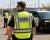 Sheriff officers wearing ANSI Class 2 reflective safety vests near a patrol vehicle.