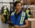 Female warehouse supervisor wearing a blue mesh safety vest while using a tablet in a distribution warehouse.