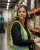 Female warehouse worker wearing 3M Peltor two-way radio earmuffs in a busy distribution warehouse.
