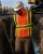 Worker wearing orange hi-vis safety vest with hood while inspecting a utility trench on a construction site.