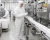 Worker wearing a white sterile coverall inspecting bottles on a vitamin manufacturing processing line.