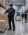 Male cold storage warehouse worker wearing a black insulated freezer jacket while stacking frozen product boxes with a forklift and other workers in the background.