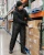 Male warehouse worker wearing black insulated freezer bib overalls while stocking boxes in a large cold storage warehouse aisle.