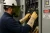 Electrician wearing flame-resistant leather gloves, arc-rated face protection, and FR clothing while testing an energized electrical panel.