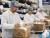 Warehouse workers wearing safety glasses, disposable lab coats, and bouffant caps while packing vitamin bottles