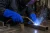 Worker wearing blue leather welding gloves while handling metal in an industrial welding shop