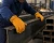 Worker wearing yellow leather work gloves while handling steel beams in a metal fabrication shop
