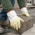 Worker wearing coated safety cuff gloves while lifting concrete block outdoors