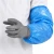 Close-up of a worker wearing a blue disposable sleeve cover and gray protective glove over a white lab coat for food processing, laboratory, pharmaceutical, and clean manufacturing work.