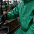 Green PVC chemical suit with attached hood and sealed seams, worn during industrial acid transfer work