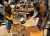 Two foundry workers wearing leather aprons, protective gloves, face protection, and safety glasses while pouring molten metal into a casting mold.