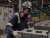 Worker wearing a full-face respirator with pink cartridges while handling concrete blocks in a cement paver manufacturing facility.
