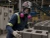 Worker wearing a full-face respirator with pink cartridges while handling concrete blocks in a cement paver manufacturing facility.