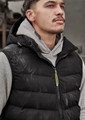 A unisex black hooded puffer vest is worn over a grey hoodie. The vest features a logo and a zip closure.