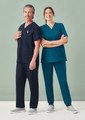 A unisex scrub top in navy and teal, worn by a male and female model, with a stethoscope and casual grey shoes.