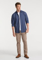 A man wears a navy long sleeve shirt with rolled sleeves, paired with light tan pants and brown boots.