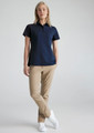 A woman in a navy short sleeve polo shirt paired with khaki trousers and white sneakers. The shirt has a logo.