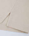 A close-up of a beige cotton/poly pique polo shirt, highlighting the stitched hem and sleeve detail.