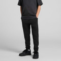 Black youth track pants featuring a fitted style and side pockets, worn with a black t-shirt and sneakers.