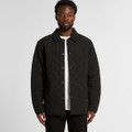 A man wearing a black quilted jacket with a button-up front and a collared neck. The jacket has a logo.