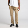 Beige pants are displayed on a model standing with hands in pockets, wearing a white t-shirt and black shoes.