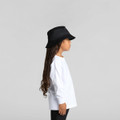 A child in a white long-sleeve tee and a black bucket hat, standing in profile against a neutral background.
