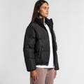 A black puffer jacket with a high collar and side pockets, worn by a model standing against a neutral background.