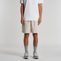 Light beige relaxed track shorts with side pockets, worn by a model standing against a plain background.