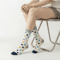 Bamboo socks in white with vibrant polka dots in blue, yellow, and grey, displayed on a seated model.