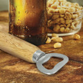 A drink bottle opener with a wooden handle and metal head, resting on a wooden surface near a bottle and peanuts.