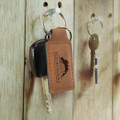 A key ring made of brown leather with a metal keychain, hanging alongside several other keys on a wooden surface.