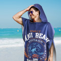 A navy blue adult hooded towel with a logo, displayed against a beach backdrop.