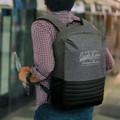 A grey and black backpack with padded straps and a logo, carried by a person in a checked shirt.