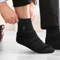 Black socks being worn, featuring a subtle logo on the side. The person is adjusting them while seated.