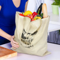 A beige tote bag filled with fresh vegetables and a baguette, featuring a logo on the front.
