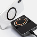 A black wireless charging power bank with a circular charging area, beside a smartphone featuring a similar design element.