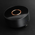 A wireless charging speaker in black with a glossy finish and a copper accent on top, featuring control buttons and a logo.