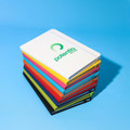 A stack of A5 notebooks in various bright colours, featuring a logo on the white cover at the top.