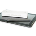 A silver metal pen rests on a tablet, next to its white packaging featuring a logo.