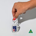A hand holds a clear tear drop acrylic keychain featuring the Australian flag. The keychain has a silver ring and a logo.