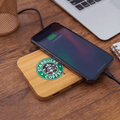 A bamboo wireless charging dock with a phone on top, featuring a logo and placed on a wooden surface.