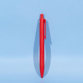 A red plastic ball pen stands upright against a light blue background, featuring a simple design and a logo.