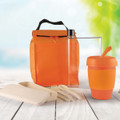 An orange picnic pack containing a drink bottle, reusable cup, utensils, and food containers, all in a vibrant setting.