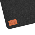 A dark felt desk mat with a stitched leather tag that reads "I used to be a plastic bottle."