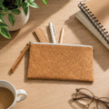 A cork pencil case with a zippered closure, surrounded by pens, a ruler, a notepad, and a cup of coffee.