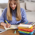 A stack of Venture Bondi A5 Notebooks in various colors, with a person writing in one of the notebooks.