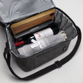 A cooler bag in grey, containing a wine bottle, a wooden item, and a rolled-up cloth with a ribbon.