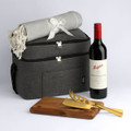 A cooler bag in grey with a blanket, a bottle of red wine, and wooden and gold utensils.