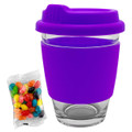 A purple glass coffee cup with a silicone lid and sleeve, accompanied by a packet of colourful jelly beans.